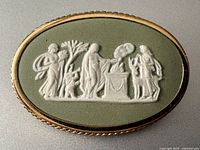 Front view of oval sage green Wedgwood jasperware brooch showing classical white relief scene and gold-tone frame