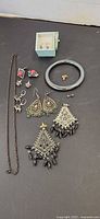 All jewelry items laid out including bangle, necklace, multiple earring pairs, single studs and small box