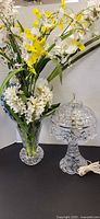 Glass table lamp with cord and cut-glass vase of artificial flowers displayed side by side