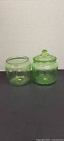 Both green depression glass cookie jars side by side showing one lid
