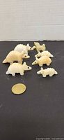 Group shot of all seven cream colored animal figurines with coin for scale