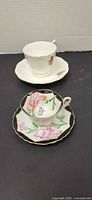 Two teacup and saucer sets displayed; front set shows Shafford lily pattern, rear set shows Royal Albert white with floral sprig