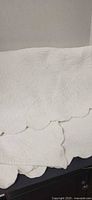 Folded white quilted bedspread showing stitched pattern and scalloped edge