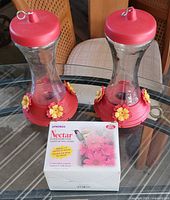 Two glass hummingbird feeders and box of nectar mix on table