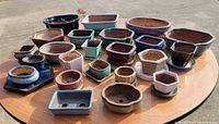 All 28 ceramic bonsai pots displayed on round table, various colors and shapes visible
