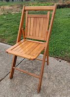 full front view of wooden folding slatted chair on pavement with grass background