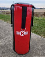 Full view of red and black Ringside punching bag standing upright on pavement