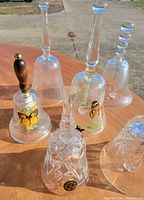All six clear glass bells on table showing varied sizes, decals and handles