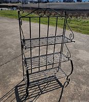 Front view of black wrought iron three-tier folding rack showing overall structure