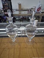 Both Stuart Crystal Ariel decanters side by side showing complete stoppers and footed bases