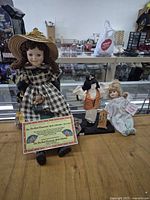 Three dolls displayed on counter: House of Lloyd Sue Ann doll, Asian style doll, baby doll