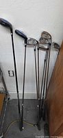 Seven clubs leaning against wall showing driver and irons