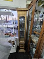 Full view of tall narrow curio cabinet beside other furniture