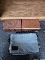 Three cassette storage cases: two brown vinyl snap-top boxes and one grey BMI nylon shoulder case