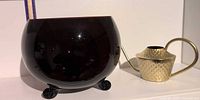 Amethyst glass bowl beside gold-tone watering can