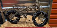 Full side view of wire motorcycle sculpture on wood base