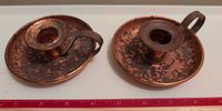 Pair of copper chambersticks side by side with measuring scale showing diameter