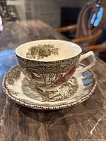 Tea cup on matching saucer showing village scene and ivy border