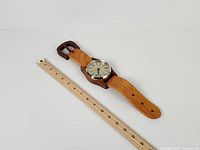 Full view of wooden wristwatch wall clock next to ruler for scale