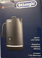 Front of sealed retail box showing DeLonghi matte black electric milk frother