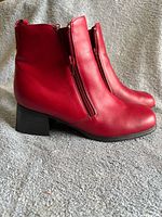 Side profile of both red ankle boots showing leather uppers, zippers and block heel