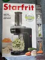 Front of sealed retail box showing appliance and spiralized vegetables