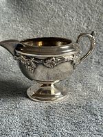 Open silver plated creamer showing grapevine border and pedestal base