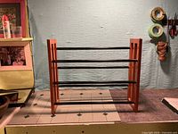 Shoe rack in compact form showing wood sides and three black metal rods