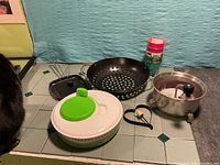 Group shot of all items: salad spinner, perforated grill pan, potato ricer, square grill pan with lid, egg mould, stack of four cups
