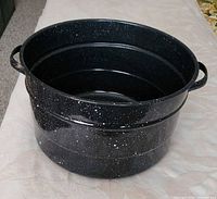 Angled view of black speckled enamel pot standing upright