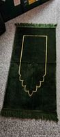 Full view of dark green prayer mat showing gold outline and fringe