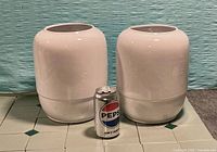 Front view of both white glazed pottery urns beside soda can for scale