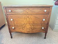 Front view of three-drawer wooden dresser showing etched design, ceramic knobs, turned legs