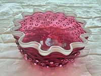 Angled view showing hobnail exterior, ruffled white rim, cranberry color