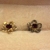 Close-up of both flower stud earrings showing gold plating and red centre stones