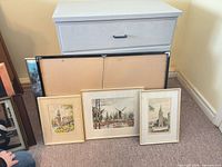 Overall view showing three small prints in cream frames, backside of large seascape poster and narrow gold-framed print