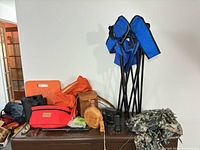 Overview showing two folded blue tripod chairs, red Winchester pack, leather canteen, binoculars, camo netting and other gear on surface
