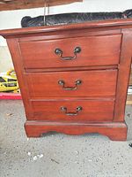 Front view showing three drawers with brass bail pulls and shaped base