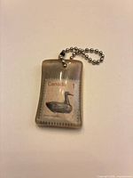 Front view showing Canadian $1 duck stamp within resin and attached bead chain