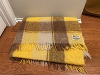 Folded yellow, brown, cream plaid mohair blanket with fringe