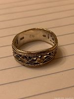 Wide band silver ring showing leaf pattern and stones on lined paper