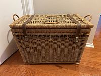 Front view of rectangular wicker basket showing lid, leather straps, and side handles