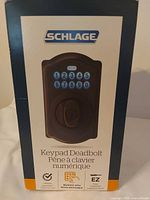 Retail box front showing Schlage keypad deadbolt, Camelot trim, aged bronze