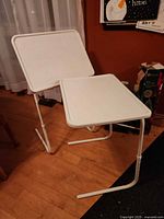 Two white adjustable tray tables showing tops and frames