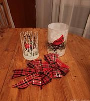 Two glass cardinal candleholders and plaid bows on table