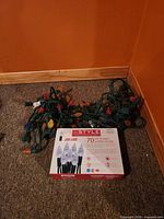 Boxed InStyle LED string light and two tangled multicolour incandescent light strings on carpet