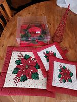 all items displayed on wooden surface: boxed candle holder set, red wire cone tree, three quilted pot holders