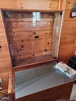 Front view of pine and glass wall cabinet on table with loose glass shelf and hardware bag visible