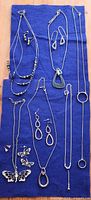 All jewelry pieces arranged on blue cloth showing necklaces, earrings, brooch and charms