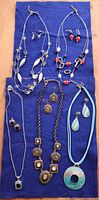 All six necklaces with corresponding earring pairs laid on blue fabric